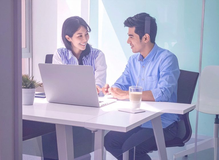 Mitarbeitende sitzen im Büro am Laptop und unterhalten sich